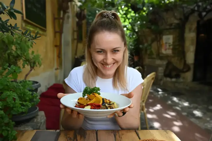 Uśmiechnięta kobieta prezentuje talerz pełen kolorowych warzyw, idealnych na dietę śródziemnomorską.