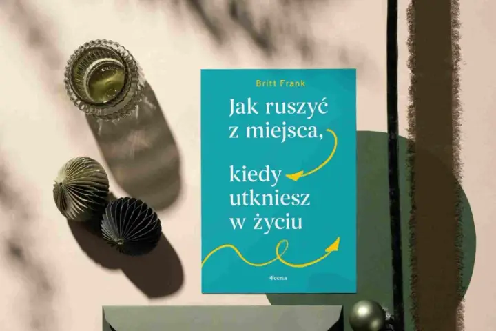 Książka "Jak ruszyć z miejsca, kiedy utkniesz w życiu" Britt Frank. Obok szklanka z napojem i ozdobne kule. Idealna lektura, gdy dopada lenistwo.