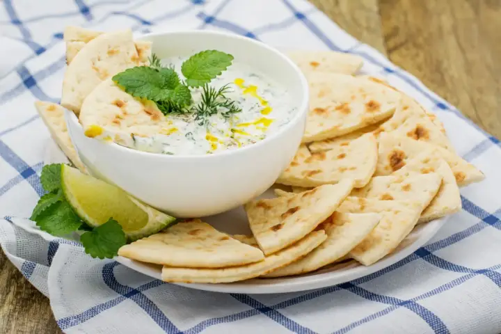 Un bol de tzatziki crémeux garni d'herbes fraîches, servi avec des morceaux de pain pita croustillants. Parfait pour tremper !