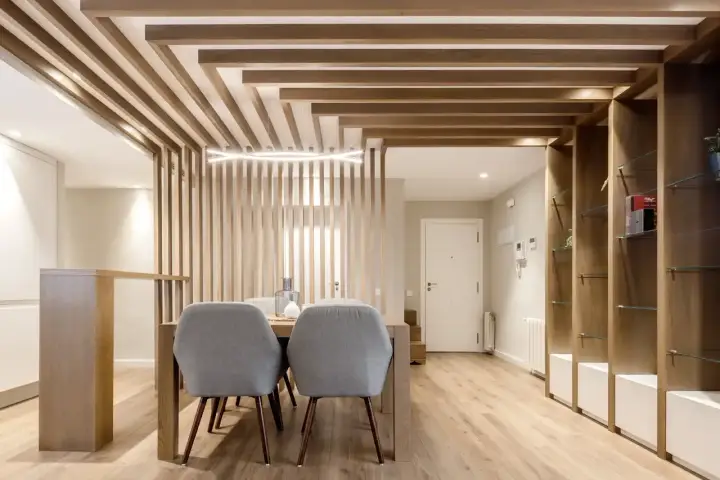 Comedor moderno con separador de listones de madera y estanterías. Preguntarse cuanto se tarda en tirar un tabique es irrelevante aquí.