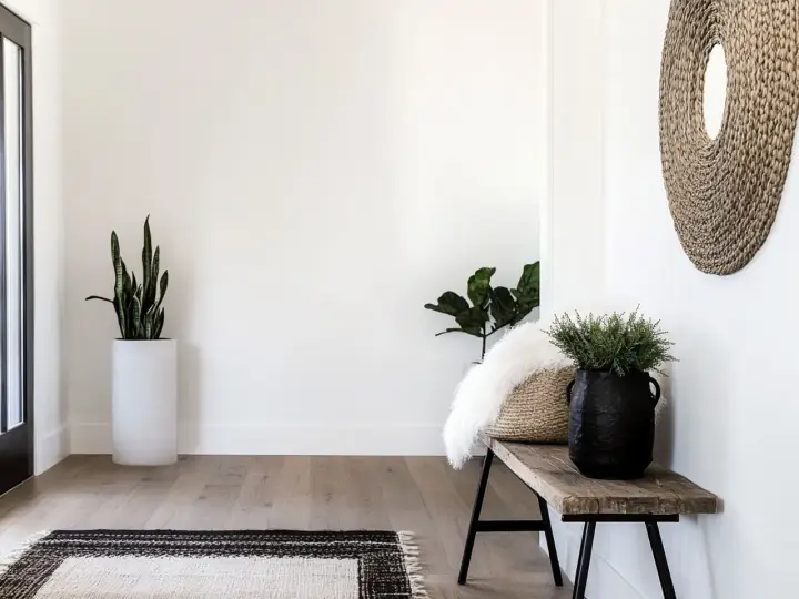 Przytulny przedpokój w stylu boho z drewnianą ławką, plecionym lustrem i roślinami.