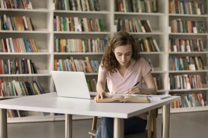 Młoda kobieta uczy się w bibliotece, zastanawiając się, czy studia chemiczne to dobry wybór.