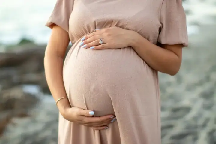 Brzuch kobiety w ciąży, delikatnie otulony dłonią. W trosce o zdrowie maluszka, przyszła mama unika stosowania retinolu w ciąży.