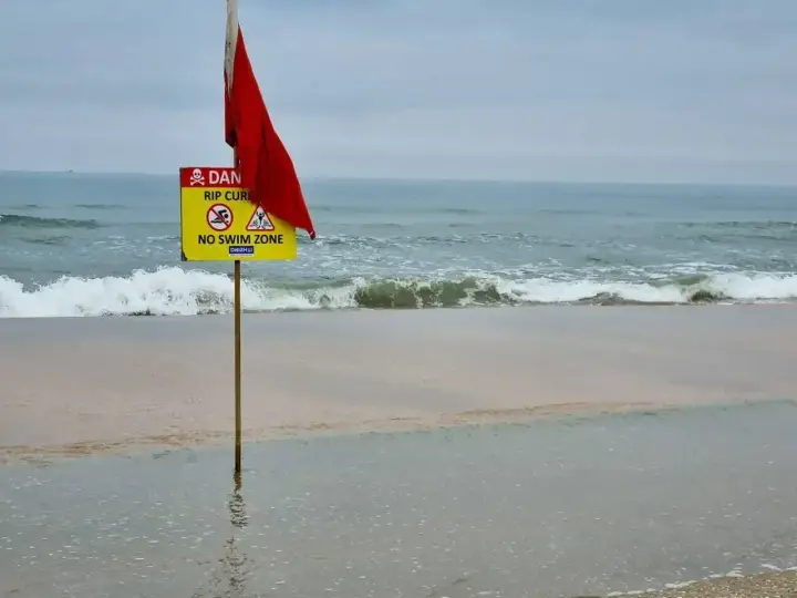 Röd flagga och skylt varnar för farliga strömmar vid stranden i Goa, Indien. Ingen badzon.
