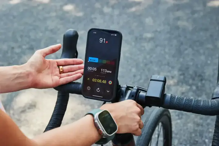 Rowerzysta sprawdza na telefonie, co oznacza puls 91. Na ekranie widać tętno 113 BPM i czas treningu.