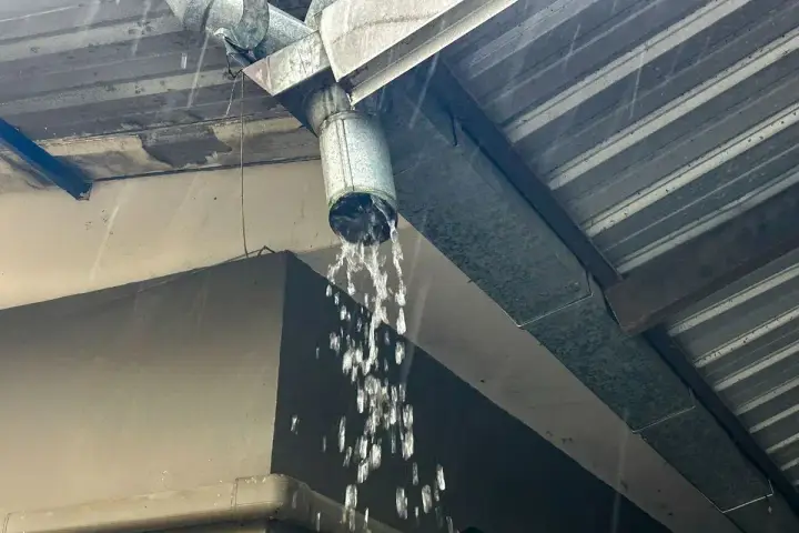 Gouttière en métal sous une pluie battante, l'eau s'écoule abondamment du tuyau, assurant l'évacuation eau de pluie.