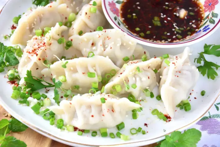 Pierożki gyoza, posypane szczypiorkiem i sezamem, podane z sosem.