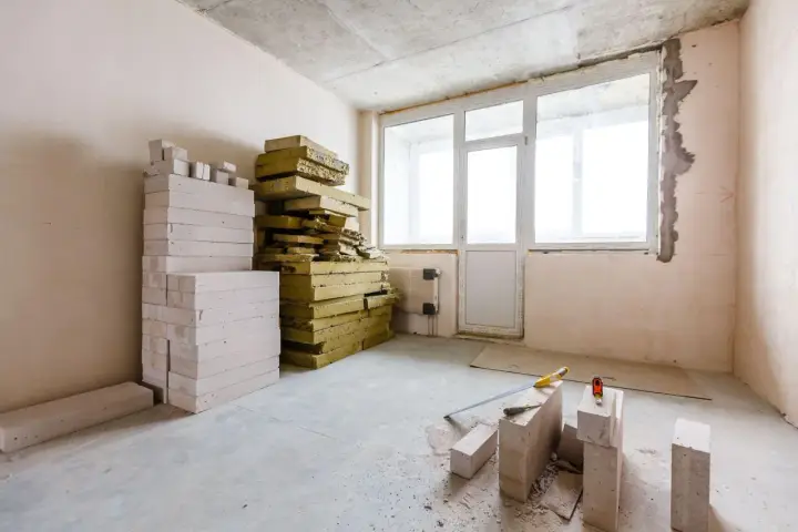 Materiały budowlane: pustaki i wełna mineralna, gotowe do ocieplenia od wewnątrz. Narzędzia budowlane leżą na podłodze.
