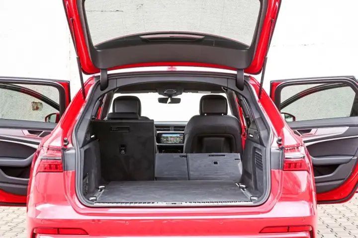 Czerwone Audi A6 Avant z otwartą klapą bagażnika i drzwiami. Wnętrze pokazuje przestronny bagażnik, idealny na wakacyjne wyjazdy, z możliwością powiększenia przestrzeni po złożeniu siedzeń.