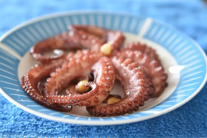 Gotowy ośmiornica przepis na talerzu z niebieskimi paskami. Delikatne macki z czosnkiem, idealne do degustacji.