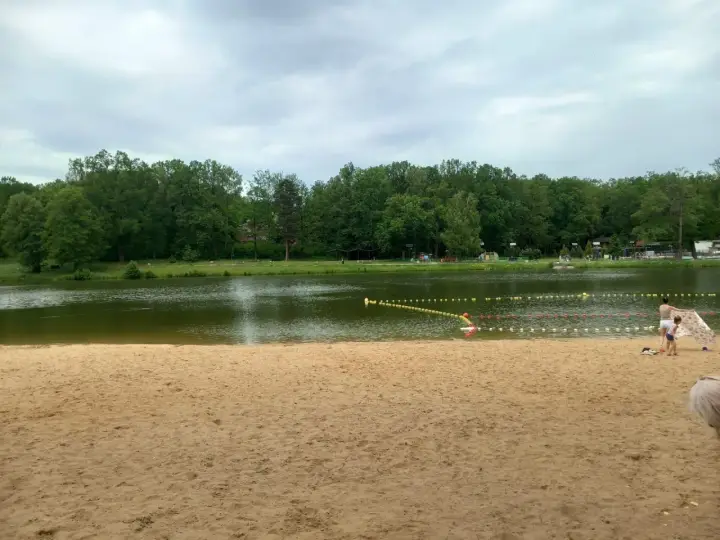 Piękna, piaszczysta plaża w Dziećkowicach zaprasza do wypoczynku nad jeziorem. W tle zielony las i spokojna woda.