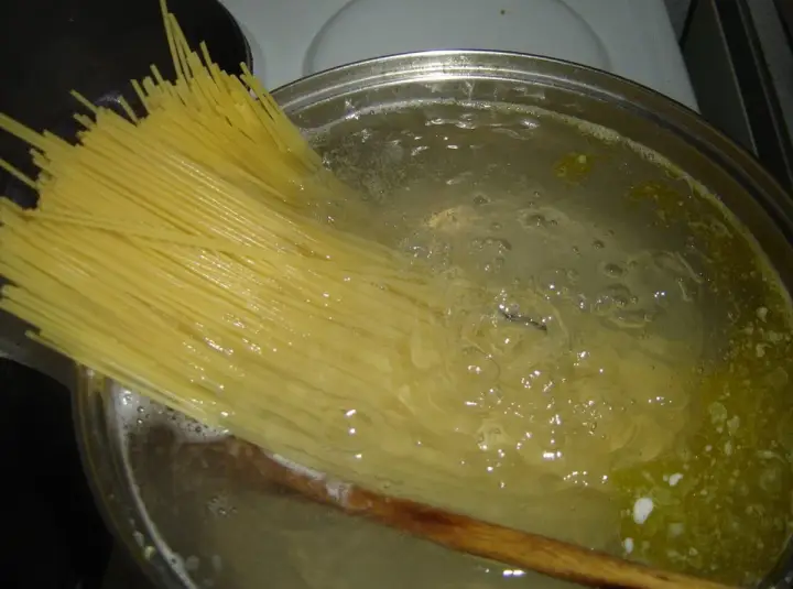 Długi makaron spaghetti zanurza się w gotującej wodzie. Czas, ile gotuje się makaron, zależy od jego grubości.