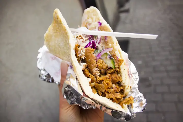 Pyszny kebab w bułce z mięsem, warzywami i sosem. To danie, które swoją popularność zawdzięcza podróżom i wymianie kulturowej, pokazując skąd pochodzi kebab.
