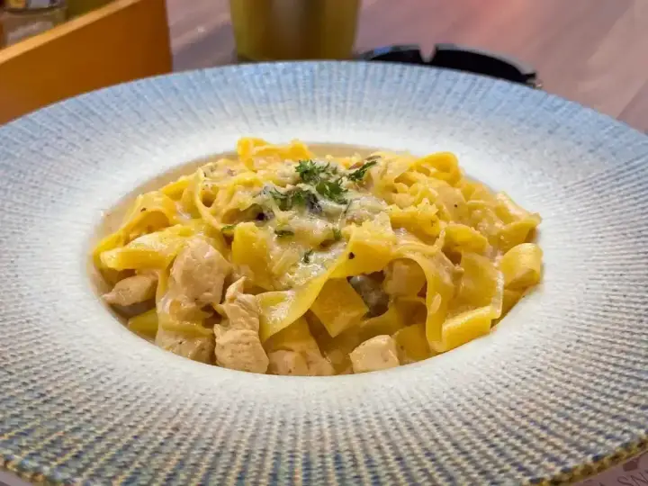 Pyszny makaron włoski z kawałkami kurczaka w kremowym sosie, posypany ziołami i parmezanem.
