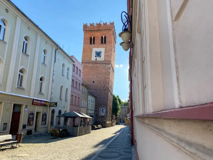 Krzywa wieża w Ząbkowicach Śląskich, ceglana, z zegarem, góruje nad brukowanym rynkiem.
