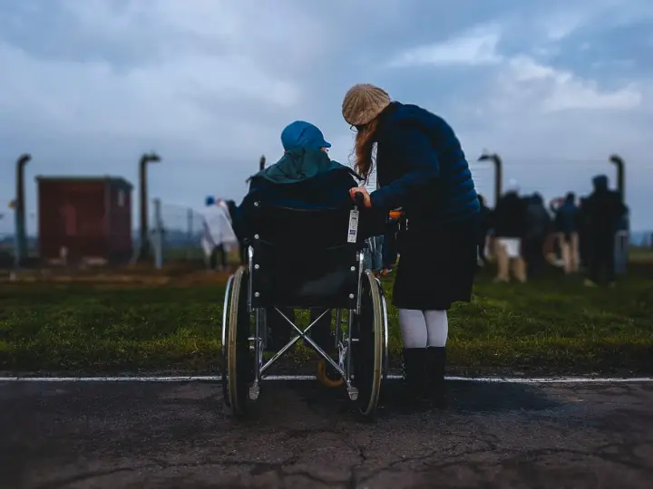 Accompagnamento anziani a chi spetta: una donna spinge una persona in sedia a rotelle, con altre figure sfocate sullo sfondo.