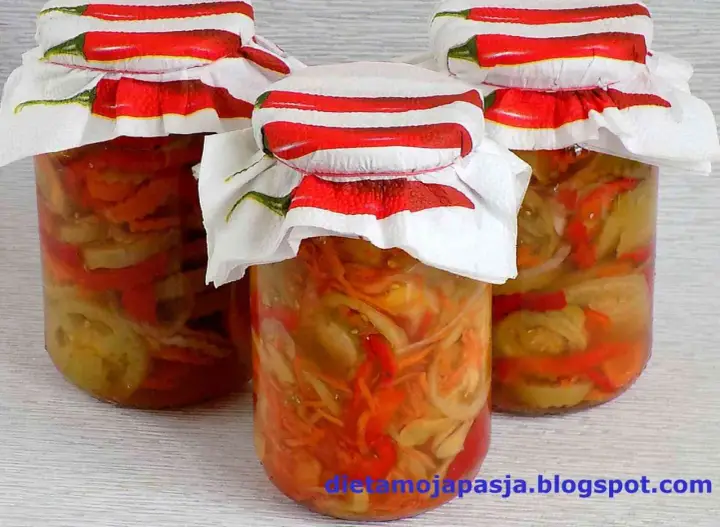 Słoiki z pyszną sałatką z pomidorów na zimę, ozdobione serwetkami z chili.