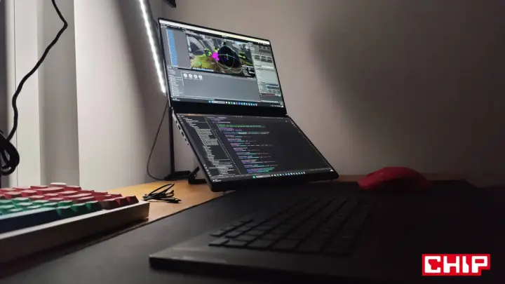 Na biurku laptop z dwoma ekranami, na górnym widać scenę w Unreal Engine 6, na dolnym kod. Obok klawiatura i czerwona myszka.
