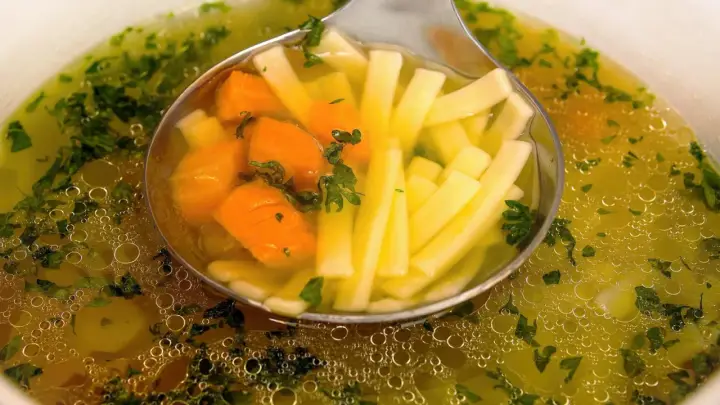 Łyżka nabiera aromatyczny bulion warzywny z marchewką i makaronem nitki.