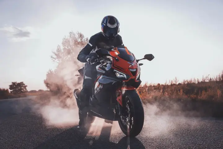 Motocyklista w kasku i kombinezonie na sportowym motocyklu, otoczony dymem. Czy motorem można jeździć po autostradzie? Tak, jeśli spełnia określone wymogi.