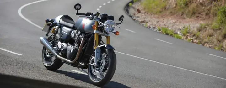 Srebrny Triumph Thruxton 900 na krętej drodze, gotowy na triumfalną jazdę.