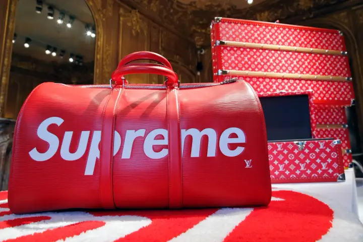 Czerwona torba podróżna z białym logo Supreme. Supreme to marka znana z limitowanych kolekcji i kolaboracji, jak ta z Louis Vuitton.