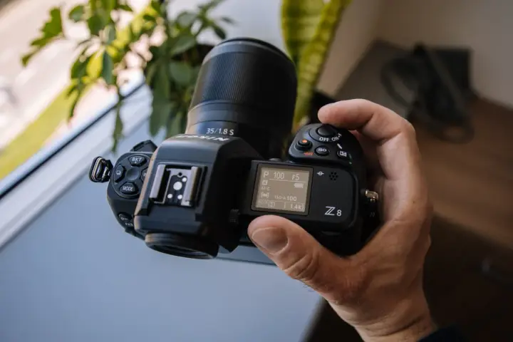 Dłoń trzyma aparat Nikon Z8 z obiektywem 35/1.8 S. Ekran pokazuje ustawienia, a cena tego modelu jest atrakcyjna.