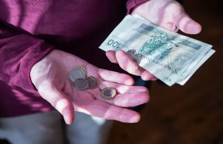 Dłonie trzymające polskie banknoty i monety. Zastanawiasz się, ile wynosi dodatek do emerytury za warunki szkodliwe?