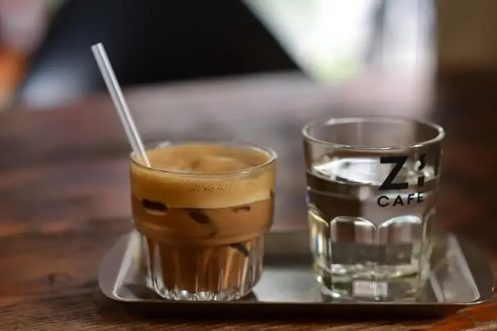 Kawa z lodem i słomką obok szklanki wody. Czy kawa jest moczopędna? Z's Cafe.