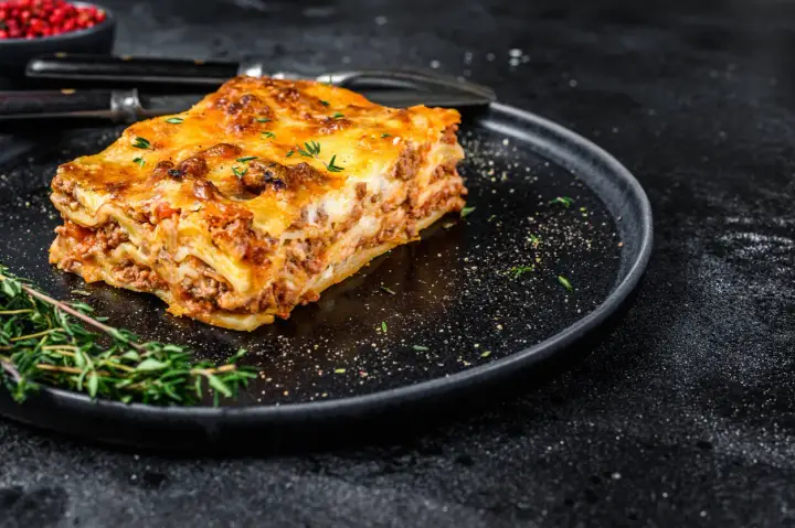 En bit gyllene lasagne på en svart tallrik, perfekt comfort food med köttfärs och ost.