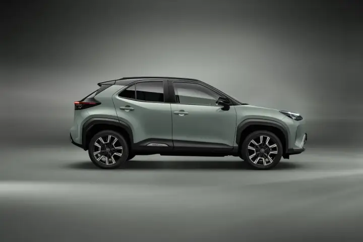 Nowy, zielony toyota crossover Yaris Cross z czarnym dachem i felgami stoi na szarym tle.
