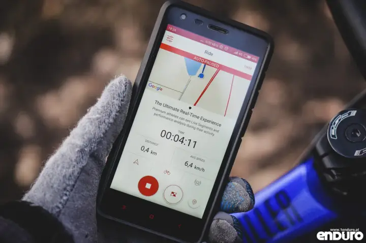 Rękawiczka trzyma smartfon z aplikacją licznik rowerowy. Widoczny czas 00:04:11, dystans 0,4 km i średnia prędkość 6,4 km/h.