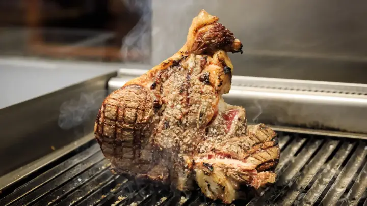 Una succulenta bistecca a Firenze, cotta alla perfezione sulla griglia, con sale grosso e fumo che sale.