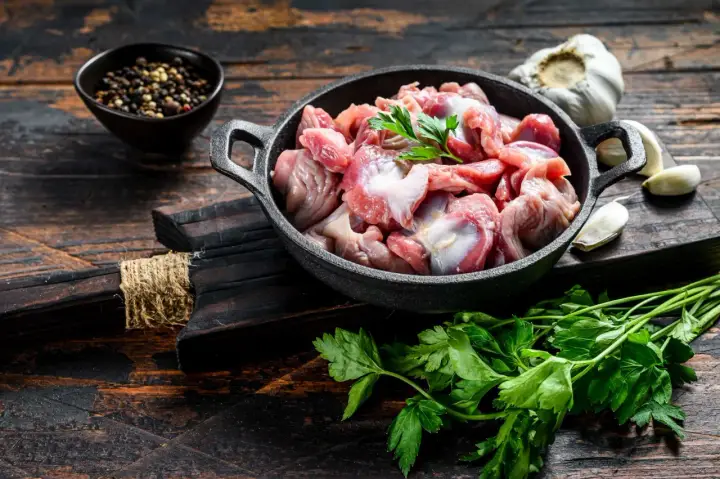 Piatto toscano con interiora di pollo crude in padella, con aglio, pepe e prezzemolo su tagliere di legno scuro.