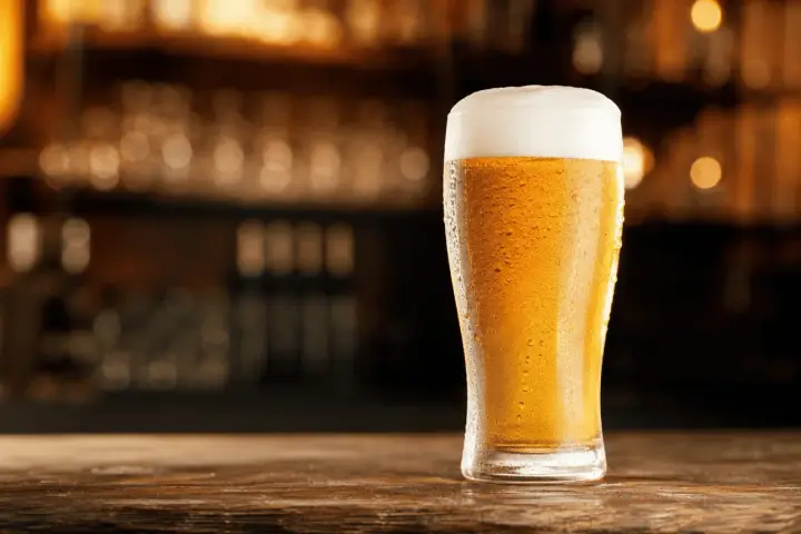 Schłodzony pilsner z obfitą pianką na blacie drewnianego baru.