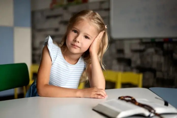 Dziewczynka z autyzmem opiera głowę na dłoni, patrząc w dal. Obok leży otwarta książka z różańcem.