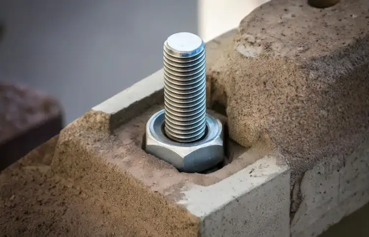 Metalowa śruba z nakrętką, czyli kotwa, mocno osadzona w betonowym elemencie.