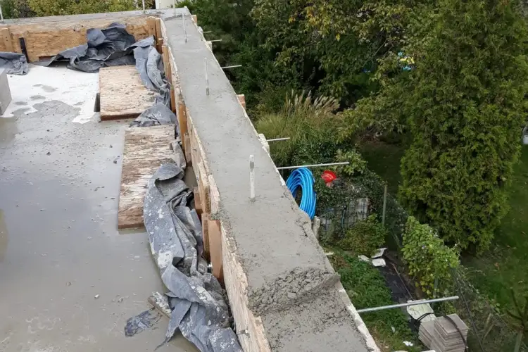 Świeżo wylana betonowa belka zbrojeniowa, co ile szpilka do murlaty. Widać drewniane szalunki i mokrą powierzchnię.