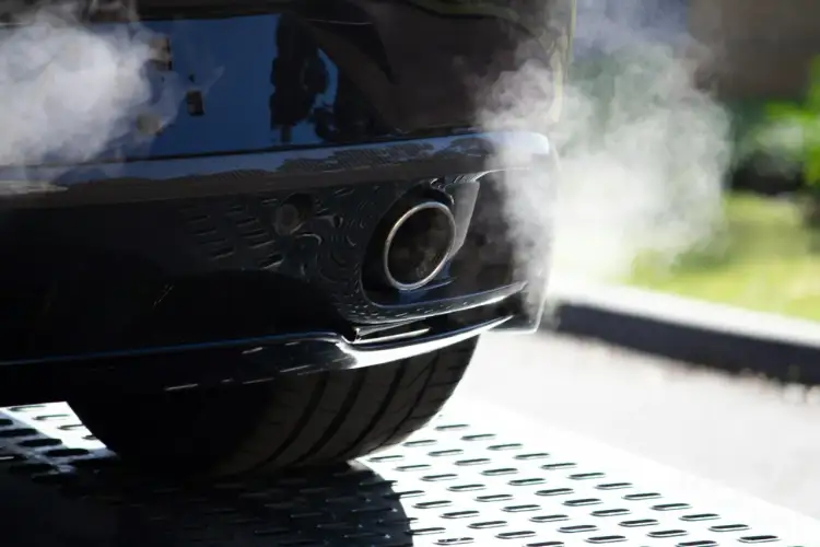 Dym wydobywa się z rury wydechowej samochodu, sugerując proces jak wypalić dpf na postoju.