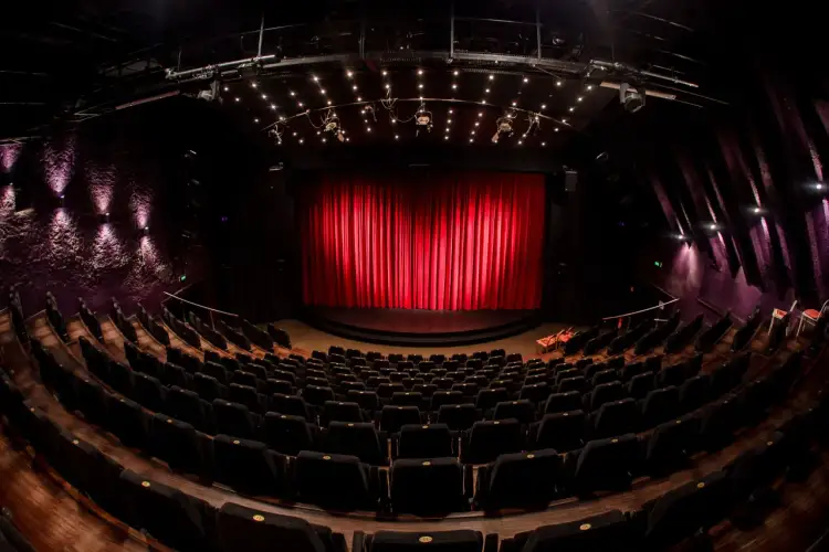 Pusta sala teatralna z czerwonymi kurtynami i rzędami czarnych foteli. Czekamy na spektakl z repertuaru Teatru Janda.