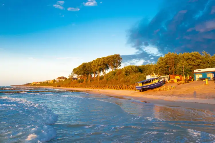 Piękny zachód słońca nad Bałtykiem. Gdzie leży ustronie? Na piaszczystej plaży z łodzią i domkami w tle.