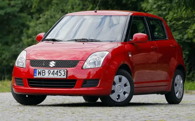 Czerwony Suzuki Swift, idealne auto do 20 tys. zł, z tablicą WB 94453, zaparkowany na zewnątrz.