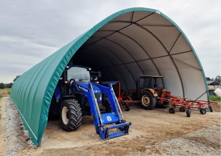 Zielona wiata bez pozwolenia wymiary chroni niebieski traktor New Holland i żółty traktor z maszynami rolniczymi.