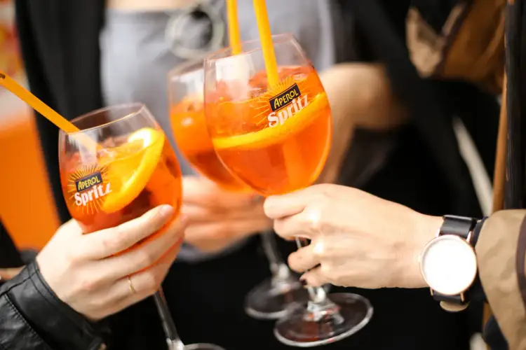 Trzy kieliszki Aperol Spritz z pomarańczą i słomką, idealne na letnie popołudnie. Tak się pije Aperol!
