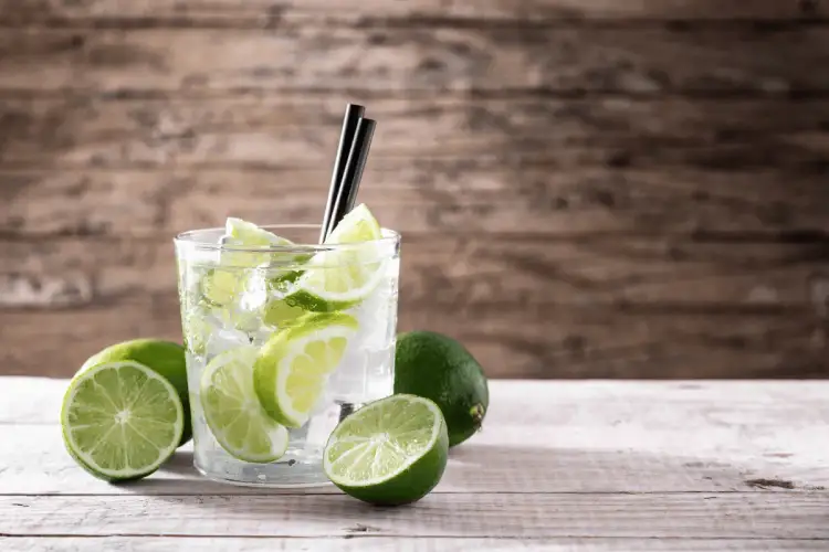 Orzeźwiający drink z limonką i lodem, otoczony świeżymi owocami. Idealny na upalne dni.