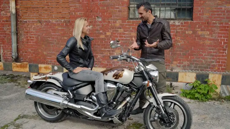 Kobieta siedzi na motocyklu Yamaha Warrior 1700, mężczyzna obok opowiada o jego możliwościach.