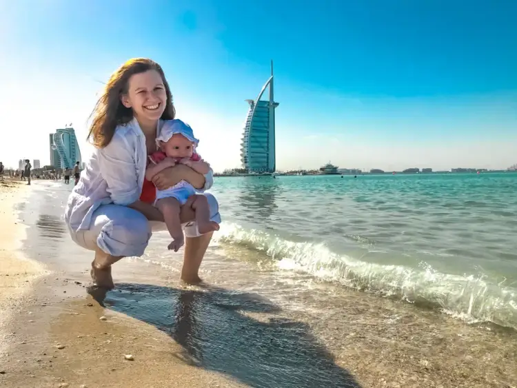 Szczęśliwa mama z dzieckiem na plaży w Dubaju, z widokiem na słynny hotel Burj Al Arab.