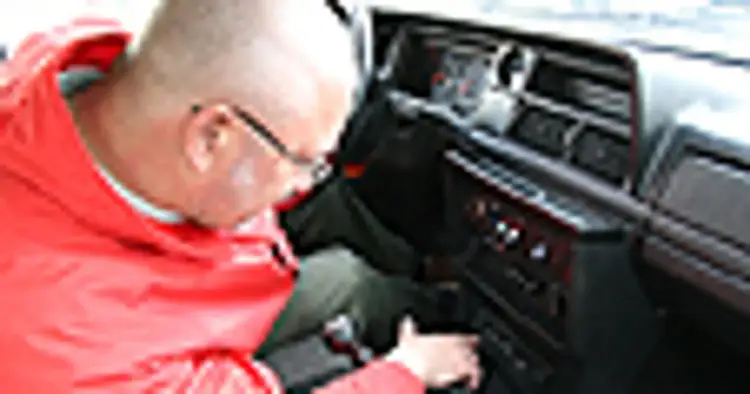 Mężczyzna w czerwonej kurtce pochyla się nad deską rozdzielczą, szukając przyczyny, dlaczego radio nie łapie fal w samochodzie.