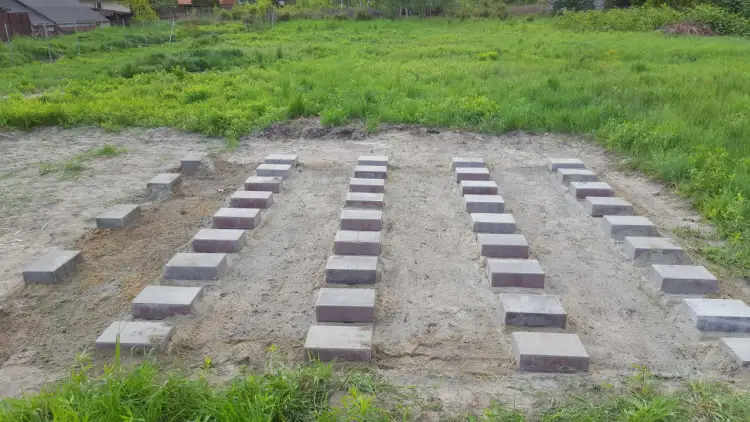 Przygotowany teren pod garaż blaszany. Ułożone bloczki betonowe tworzą fundament.