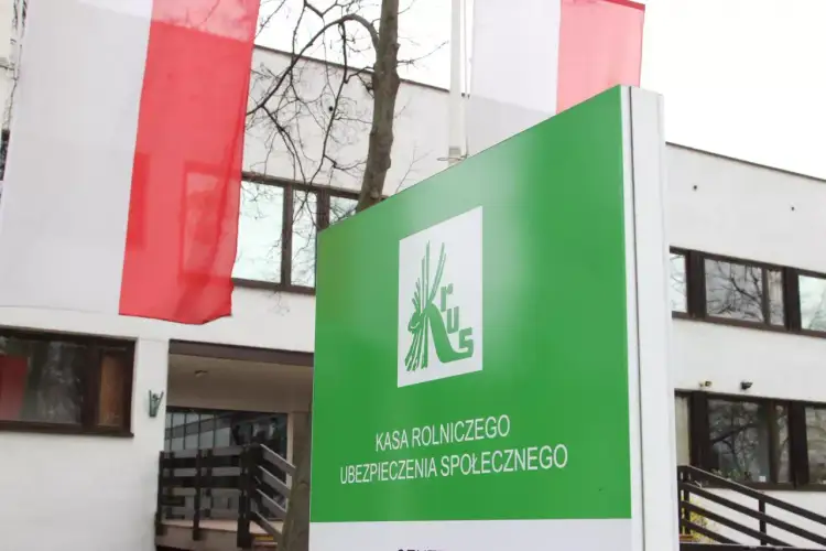 Zielony znak Kasy Rolniczego Ubezpieczenia Społecznego, gdzie można uzyskać ubezpieczenie chorobowe. W tle polskie flagi.